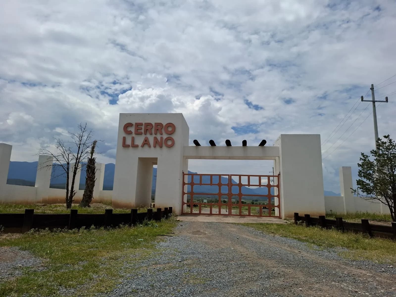 Acceso al fraccionamiento campestre Cerro Llano, con el letrero del desarrollo y la sierra al fondo